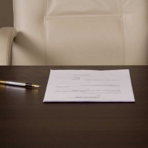 a piece of paper and a pen sitting on a desk with an empty chair behind the desk