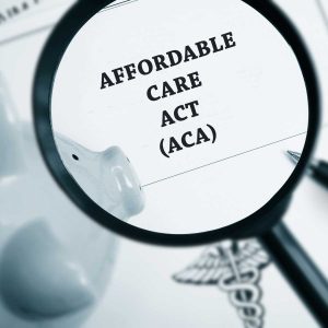 a magnify glass over a black and white paper that states affordable care act (ACA) and a piggy bank, pen, and healthcare imagery