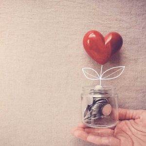a hand holding a clear glass jar of coins with an illustrated heart and plant stem growing out of it