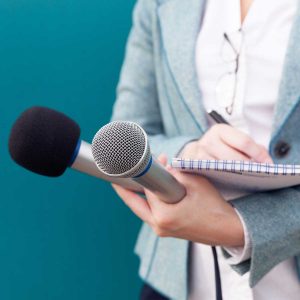 News reporter or TV journalist at press conference, holding microphone and writing notes 