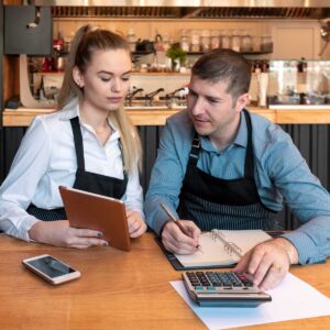New small business owners counting revenue and expenses - Start-up entrepreneurs, woman and man, businessmen doing accounting with calculator and tablet in Restaurant