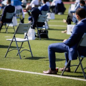 People sit on chairs apart one from another to maintain the social distance during the Covid-19 outbreak at an outdoor event on the turf of a stadium.