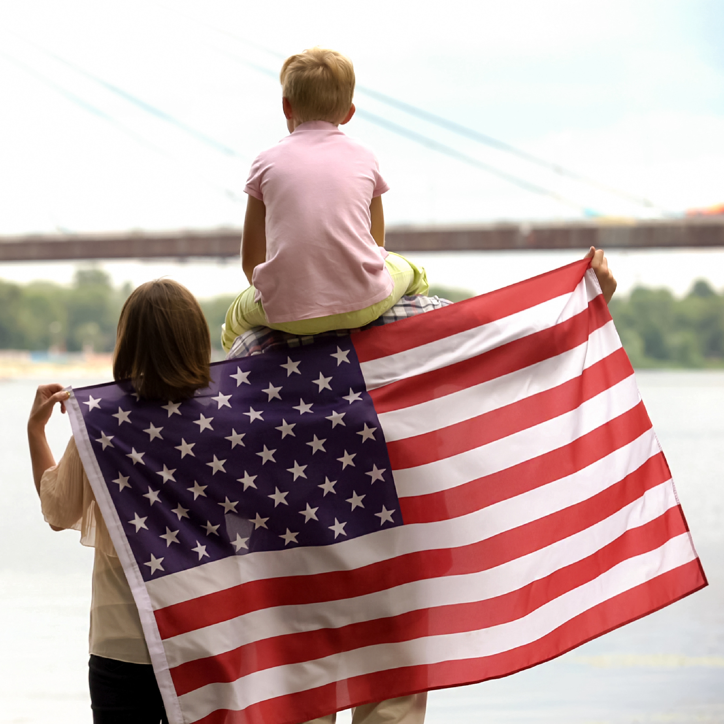 Family wrapped in American flag looking at bridge, immigration for better life