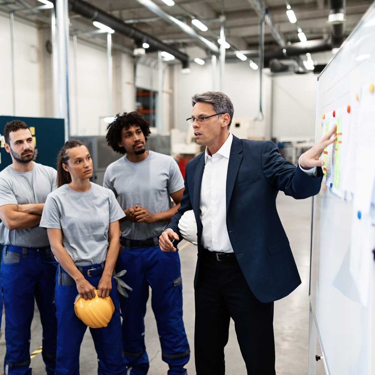 Mature businessman explaining new strategy plans to group of employees in a factory.