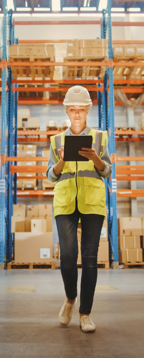 Worker Wearing Hard Hat Checks Stock and Inventory with Digital Tablet Computer Walks in the Retail Warehouse