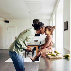 mom and her little girl having a snack at home; loving mother kissing little daughter who is sitting on kitchen counter with snack of pears next to her