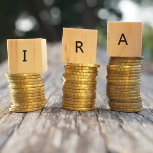 Close up of stacking gold coins and wooden blocks written IRA on nature background and natural lighting. Individual Retirement Account concept