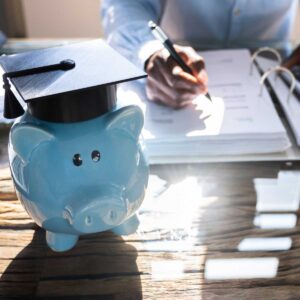 Student Loan. Accounting Advisor concept; image of a blue piggy bank with a graduation cap on it as the main focus with a businessman in the background calculating rates on a note pad