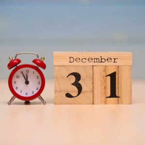 December 31st set on wooden calendar and red alarm clock with blue background.