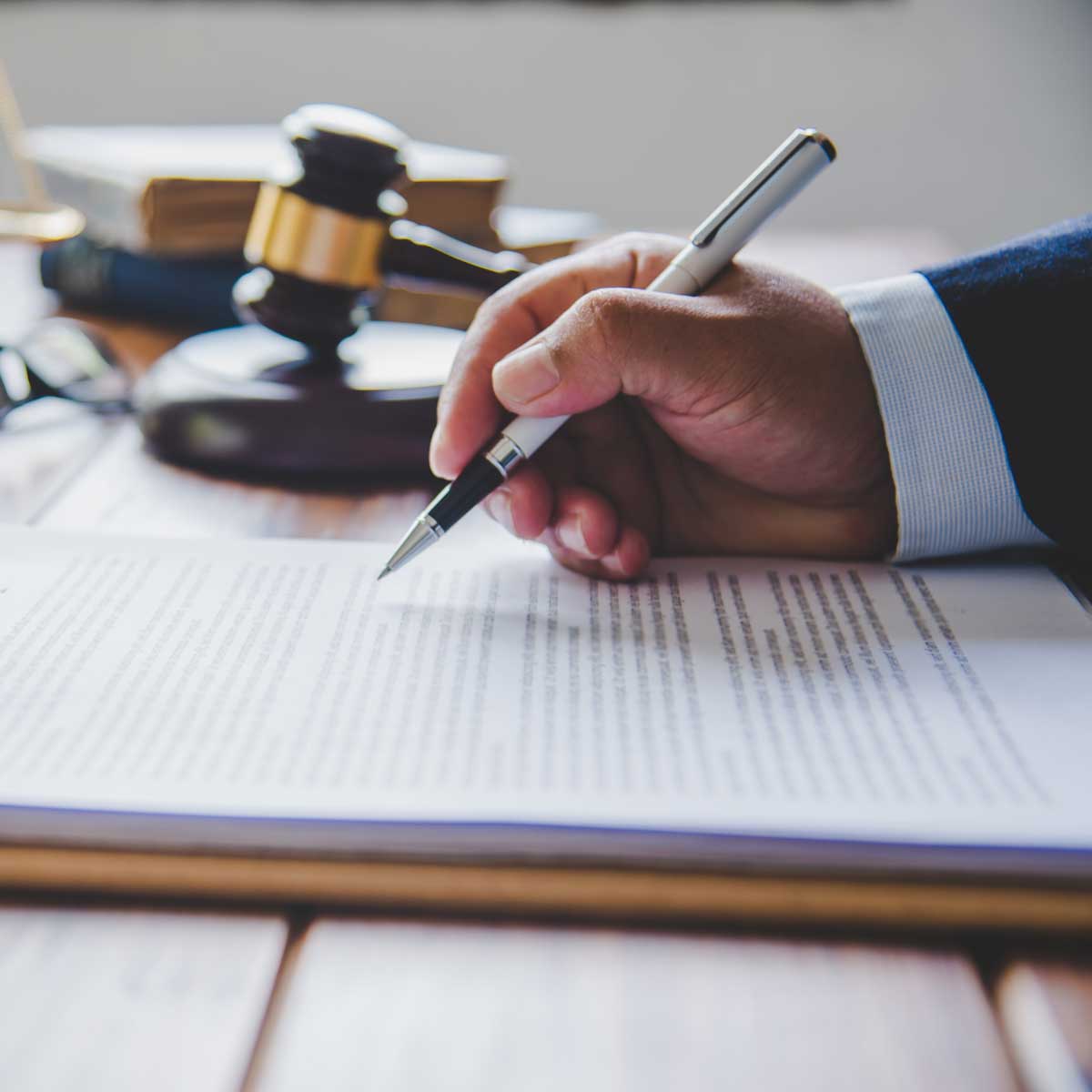 Law theme, mallet of the judge, law enforcement officers, evidence-based cases, and documents taken into account; image of a professionals' hand holding a pen over a legal document