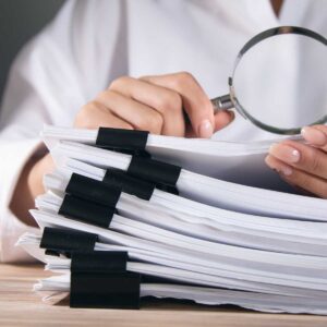 woman holding magnifying glass and large stack of documents
