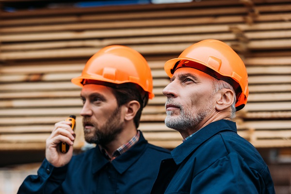 two builders in helmets working with walkie talkie outside on construction