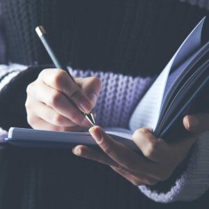 close up of a woman's hand writing a checklist down on a notepad she's holding open with her other hand