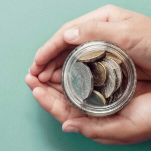 hands holding money jar full of coins in front of a seafoam green background; economic stimulus and saving concept, Coronavirus economic stimulus rescue package imagery