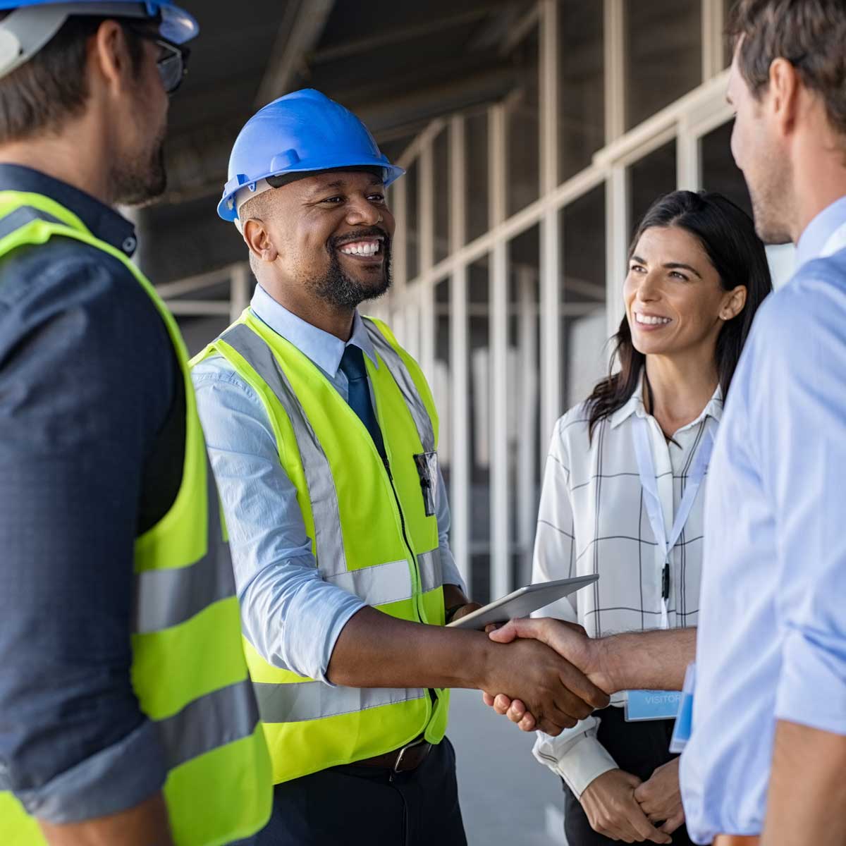 Contractor in construction and supportive employer handshake at construction site when discussing retention strategies for employees; image of four people, two of which are contractors, the other two are in business attire