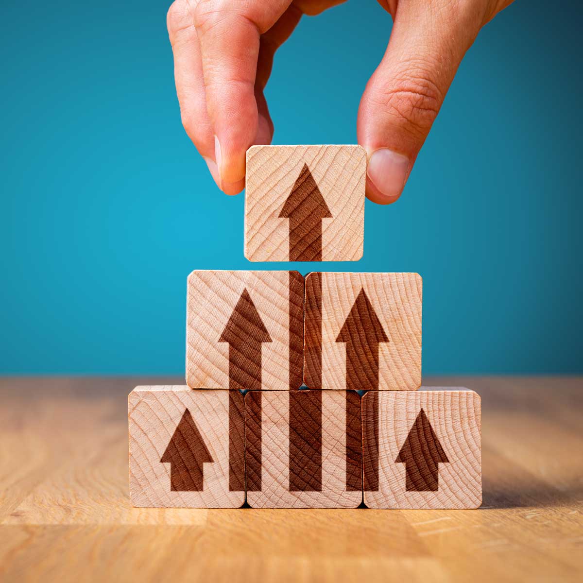 Business improvement, personal development and growth concept. Benchmarking concept. Wooden building blocks stacked on top of each other with arrows pointing upward; hand reaching for top block.