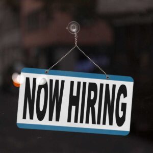 Now hiring sign hanging on a glass door