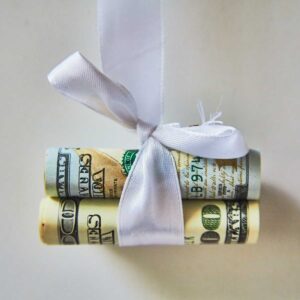 dollar banknotes, rolled up in a tube, tied with a white ribbon, like a gift, lie on a white background