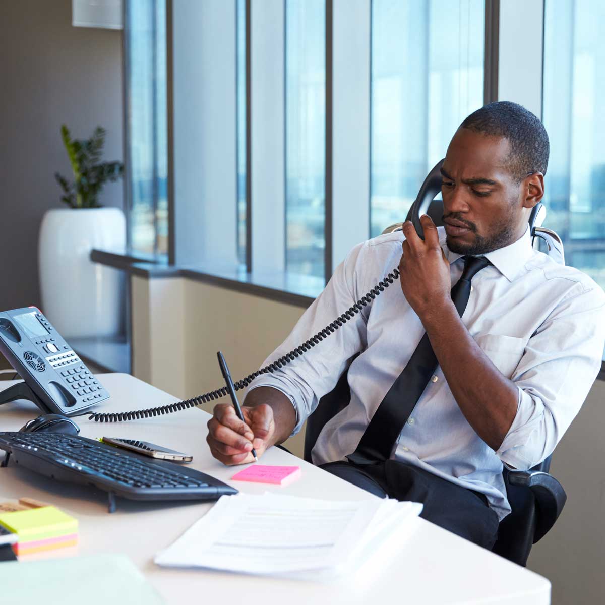 Businessman-Making-Phone-Call-Sitting-At-Desk-In-Office