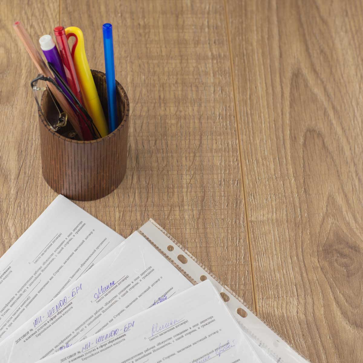 employee contracts and agreements signed and positioned in the corner of the image. cup of pens and pencils near by on wooden desk