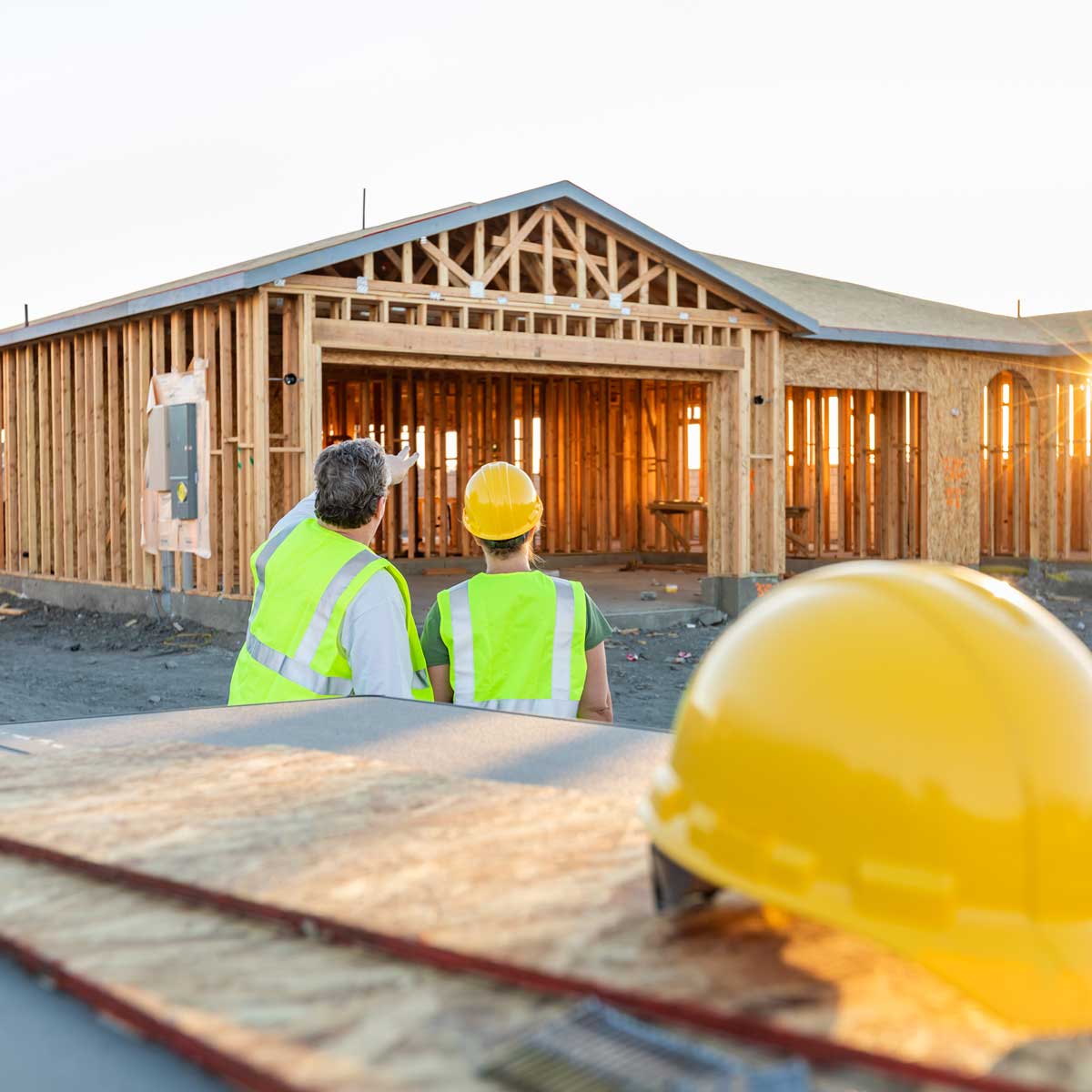 Male and Female Construction Workers observing New Home Site construction in bright outdoor lighting. wood pieces and construction hat out of focus