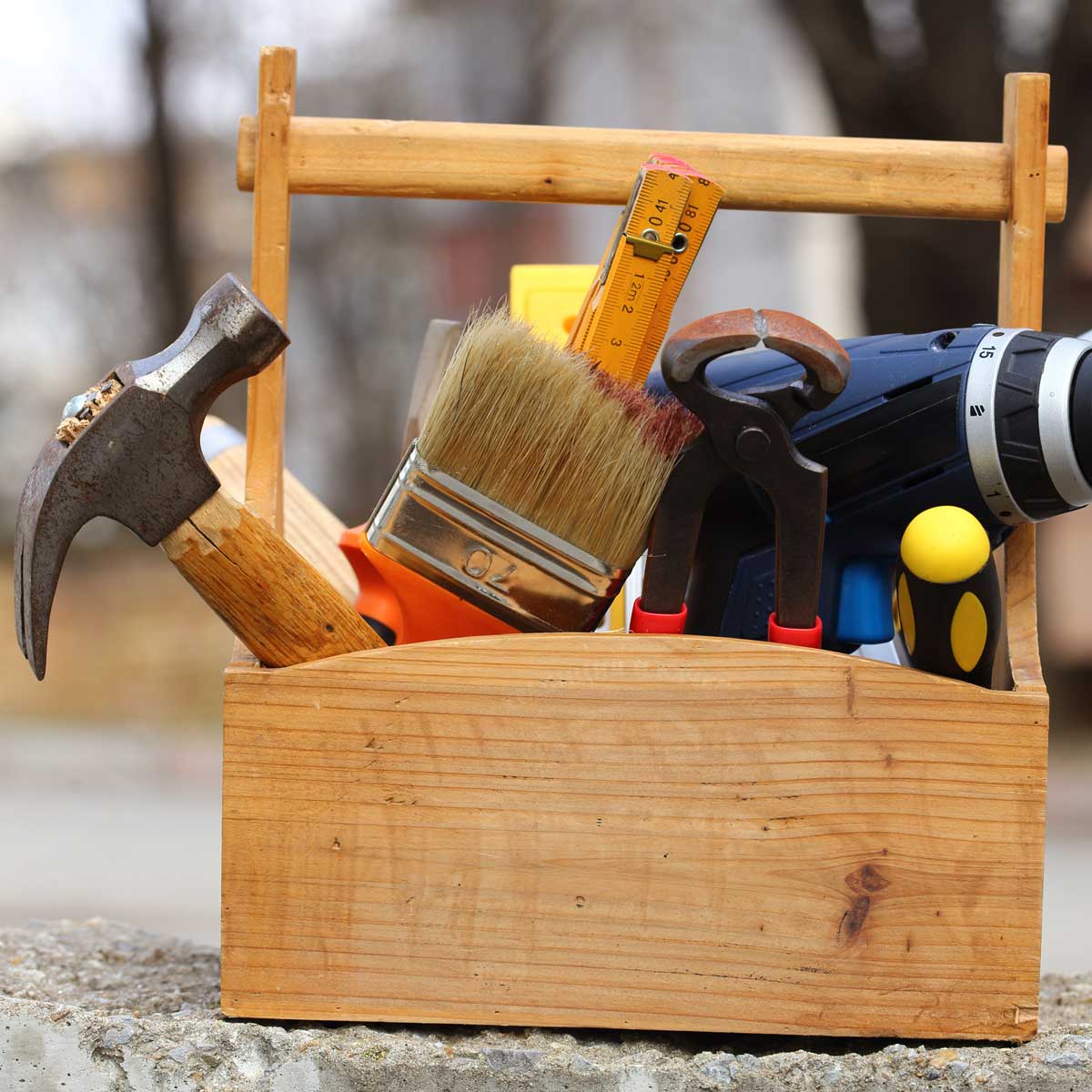 a toolbox on a background of a blurred work site. within the toolbox rests a hammer, paint brush and other tools